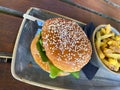 Close up of isolated beef burger with sesame bun and bowl of french fries on table
