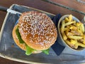 Close up of isolated beef burger with sesame bun and bowl of french fries on table