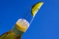 Close up of isolated bottleneck with sparkling yellow beer and a slice of lime against cloudless deep blue sky Royalty Free Stock Photo
