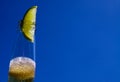 Close up of isolated bottleneck with sparkling yellow beer and a slice of lime against cloudless deep blue sky