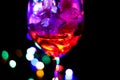 Close up of isolated red cocktail glass with ice cubes. Black background with colorful vibrant bokeh from electric light Royalty Free Stock Photo