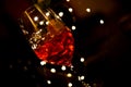 Close up of isolated red cocktail glass with ice cubes. Black background with colorful vibrant bokeh from electric light