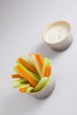 Close up isolated shot of a mixed bowl of crunchy orange carrot slices and juicy green celery sticks with a white cup of blue