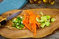 Close up of isolated sliced fresh spring onions scallions, carrots, cucumbers on wooden olive tree cutting board and japanese Royalty Free Stock Photo