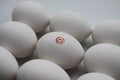 Close up of isolated white raw egg with painting of red smiling face surrounded by group of equal eggs focus on face Royalty Free Stock Photo