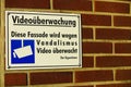 Close up of isolated white sign on red Brick wall. German text: VideoÃÂ¼berwachung. Diese Fassade wird wegen Vandalismus ÃÂ¼berwacht