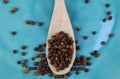 Close up of isolated wood spoon with red and black cambodian kampot pepper corns on blue old scratched china dish Royalty Free Stock Photo