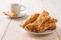 Close-up of Italian crispy bakery Sfogliatine glassate on a white saucer and cup of hot coffee over white wooden table. Sweet