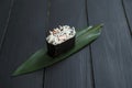 Close up of Japanese Gunkan Maki Sushi roll with snow crab and tobiko caviar on bamboo leaf on black wooden board.