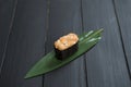 Close up of Japanese Gunkan Maki Sushi with salmon on bamboo leaf on black wooden board.