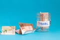 close up of a jar with travel label filled with paper money euro and other money on the side, blue background Royalty Free Stock Photo