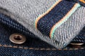 Close up of jeans fragment with button. Denim texture. Selvage.