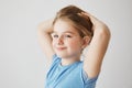 Close up of joyful little girl in blue t-shirt looking at camera, brightfully smiling and holding blonde long hair with Royalty Free Stock Photo