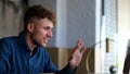 Close up of joyful young Caucasian man smiling and waving hand looking at laptop screen and video chatting online in Royalty Free Stock Photo