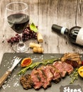 Close-up of juicy beef steak striplon with a bottle and a glass of red wine on a black stone plate on a wooden table. Royalty Free Stock Photo