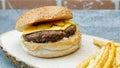 Juicy cheeseburger with  cheddar cheese, russian salad, french fries, tomato, and cucumber pickle on a natural wooden tray Royalty Free Stock Photo