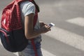 Close-up on kid with backpack using smartphone while walking through crosswalk