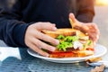 Close-up kid girl hand eating hamburger with ham and fresh vegeatables at cafe on bright sunny day outdoors. Fast food children Royalty Free Stock Photo