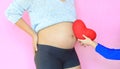 Close-up kid hand giving red heart for pregnant mother on pink background. Close up child holding red heart pillow near belly of Royalty Free Stock Photo