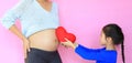 Close-up kid hand giving red heart for pregnant mother on pink background. Close up child holding red heart pillow near belly of Royalty Free Stock Photo