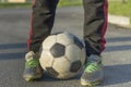 Close-up of kid legs in sportive footwear holding soccer ball outdoors on sunny day. Teenager vacations activity, sport training Royalty Free Stock Photo