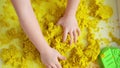 Close up of kids hands playing with yellow magic sand, top view. Development of fine motor skills, early education