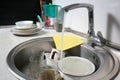 Close-up of a kitchen sink with dirty dishes in a home interior. Water flows from an open tap