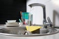 Close-up of a kitchen sink with dirty dishes in a home interior. Water flows from an open tap