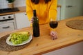 Close up of kitchen table with bottle, glass of red wine and fruits on plate. Body part of unrecognizable woman near Royalty Free Stock Photo