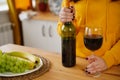 Close up of kitchen table with bottle, glass of red wine and fruits on plate. Body part of unrecognizable woman near Royalty Free Stock Photo