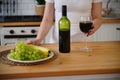 Close up of kitchen table with bottle, glass of red wine and fruits on plate. Body part of unrecognizable woman near Royalty Free Stock Photo