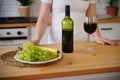 Close up of kitchen table with bottle, glass of red wine and fruits on plate. Body part of unrecognizable woman near Royalty Free Stock Photo