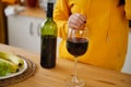 Close up of kitchen table with bottle, glass of red wine and fruits on plate. Body part of unrecognizable woman near Royalty Free Stock Photo