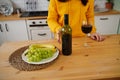 Close up of kitchen table with bottle, glass of red wine and fruits on plate. Body part of unrecognizable woman near Royalty Free Stock Photo