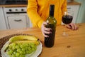 Close up of kitchen table with bottle, glass of red wine and fruits on plate. Body part of unrecognizable woman near Royalty Free Stock Photo