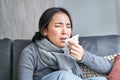 Close up of korean girl sneezing in napking, sitting at home in scarf, feeling unwell, concept of winter, heating cost