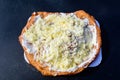 Close up of a langos, typical Hungarian food specialty, with sour cream and cheese on a white dish on a dark black table, deep fri