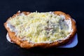 Close up of a langos, typical Hungarian food specialty, with sour cream and cheese on a white dish on a dark black table, deep