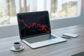 Close up of laptop computer with falling red crisis forex chart on screen, coffee cup and notepad. Wooden desk and city view Royalty Free Stock Photo