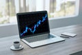 Close up of laptop on desktop with coffee cup, notepad and glowing candlestick forex chart hologram on blurry background. Trade