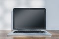 Close up of laptop with empty mock up screen placed on wooden desk. Concrete wall with shadows in the background. Royalty Free Stock Photo