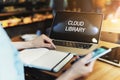 Close-up of laptop with inscription on monitor- cloud library on wooden table, in front of which sits girl with smartphone in hand