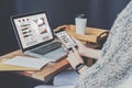 Close-up of laptop on wooden table and smartphone with graphs, diagrams and charts on screen in hands of businesswoman.