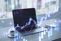 Close up of laptop at workplace with coffee cup, supplies and glowing candlestick forex chart on blurry backdrop. Technology, Royalty Free Stock Photo