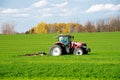 Close-up larger farm tractor with rotary cutter trailer on farmland meadow field, colorful fall foliage, cloud blue sky South Royalty Free Stock Photo