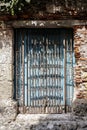 Close-up of a latticed window closed by blue wooden shutter in light and shadow, framed with stone and bricks in Old Town,