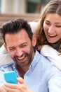 Close up laughing couple sitting together in embrace with mobile phone Royalty Free Stock Photo