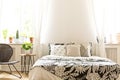 Close-up of leaf pattern black and white covers on a bed in a sunny bedroom interior. A rattan and metal chair and a stool with Royalty Free Stock Photo