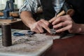 Close up of leather craftsman hands working with natural leather using hammer. Handbag master at work in local workshop. Male