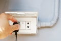 Close up left hand of man is holding black plug and prepare for battery charging a mobile phone on the electric socket on the gray Royalty Free Stock Photo